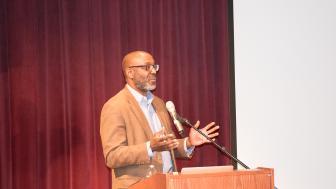 Trent Masiki speaks at a podium on the theater stage.