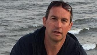 Scott Loring Sanders at the beach with water behind him.