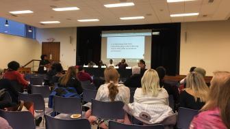 View from rear of the room of the panelists, audience and powerpoint slide.