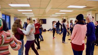 Professor watches as students dance in swing dance class in dance studio.