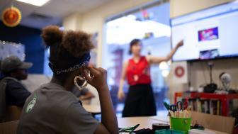 Back of a teenage girl's head with someone teaching in the background.