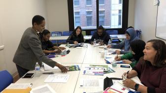 A group of people sit around a table with paper materials on it.