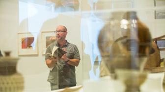 Artsy pick of Aaron Smith reading from a book, taken through a glass case at a museum.