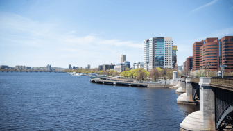 Photograph of the Charles River with blue sky and blue water and buildings of Cambridge in the background.