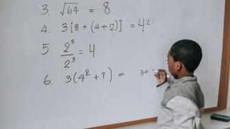 Small Black child doing a math problem at a whiteboard