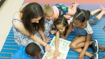 Teacher and students in the classroom, reading a book on the floor 