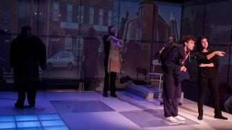 Actors on stage during a performance with dark lights and projections