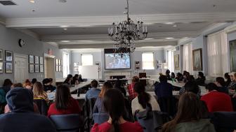 A photo of a large audience in Alumni Hall listening to a panel of speakers during the day.