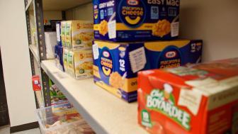 A set of shelves with macaroni and cheese and noodles stacked up on top of one another in a food pantry.