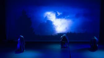 A photograph of the Marran Theater stage during a dress rehearsal of the Oxford Street Players porduction of Macbeth with three witches in front of a screen of blue clouds