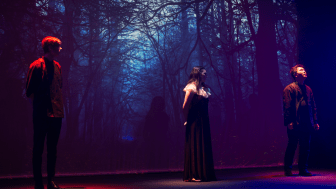 Three actors on stage against the backdrop of the woods in a production of Macbeth