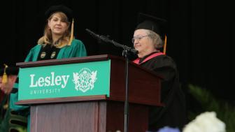 Two women standing on a stage wearing graduation gowns