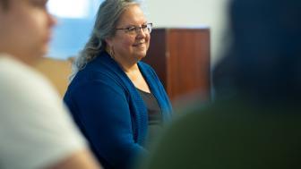 Woman with glasses and a blue sweater seated and speaking to a crowd of students