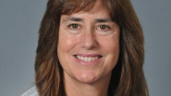 Photo of Stacey smiling against a gray background
