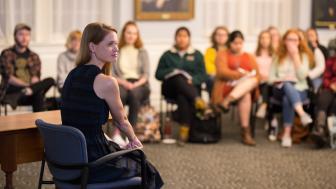 A women with long red hard sitting in a chair speaking to an audience of students