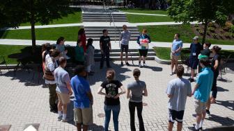 Students standing outside on the quad in a circle on a sunny summer day