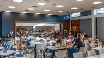 Students in the renovated dining hall sitting in chairs and getting food in a buffet line.