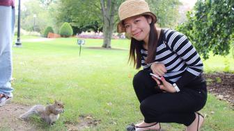 Photograph of young women wearing a hat and a striped shirt leaning down to look at a rabbit outside.