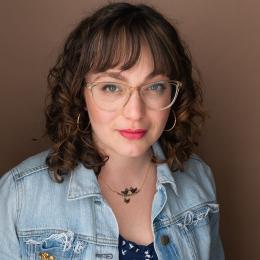 photo of faculty member Cassie Seinuk in a jean jacket and glasses against a brown background