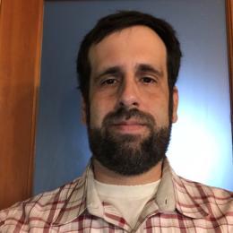 Headshot of Edward Yates. Edward has short brown hair and a beard. He wears a plaid flannel.