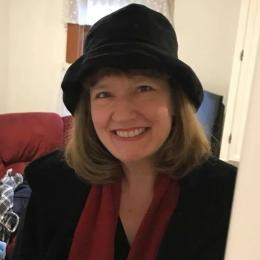 Photo of Ellen Lewis smiling, wearing a black hat, black shirt and red scarf