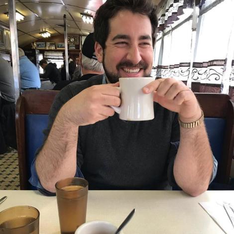 Alex in a diner smiling and holding a mug