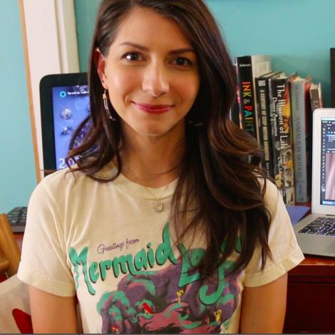 Becky smiling in t-shirt that says "Mermaid" with books and a laptop in the background