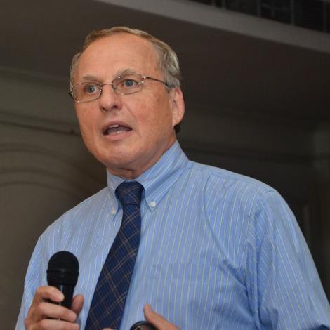 Jared Kass wearing blue collared shirt with tie speaking into a microphone