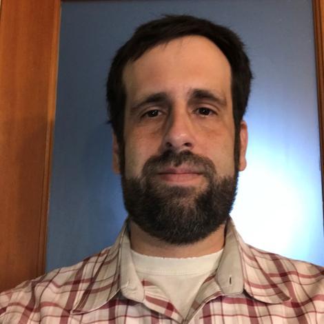 Headshot of Edward Yates. Edward has short brown hair and a beard. He wears a plaid flannel.