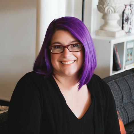 Headshot of Heather O'Neill smiling. She has purple hair and glasses.
