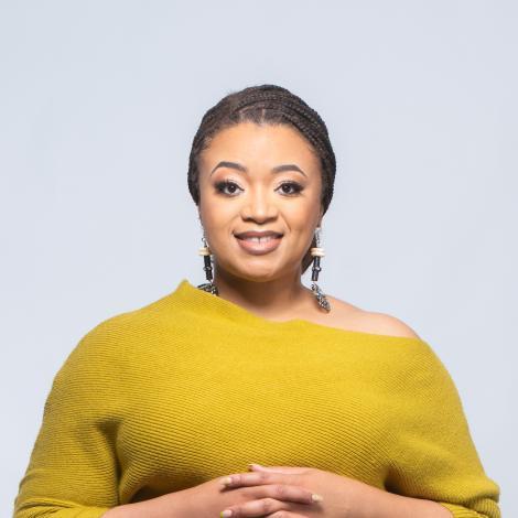 Myisha wearing a yellow shirt in front of white background with her hands intertwined