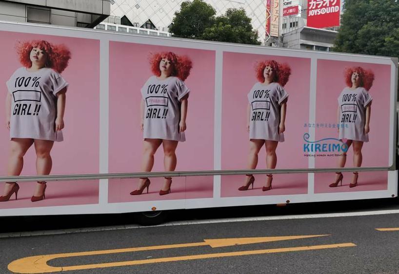 An advertisement on an 18-wheeler with a woman with red hair and a shirt that says 100% girl. Repeated four times on the truck.