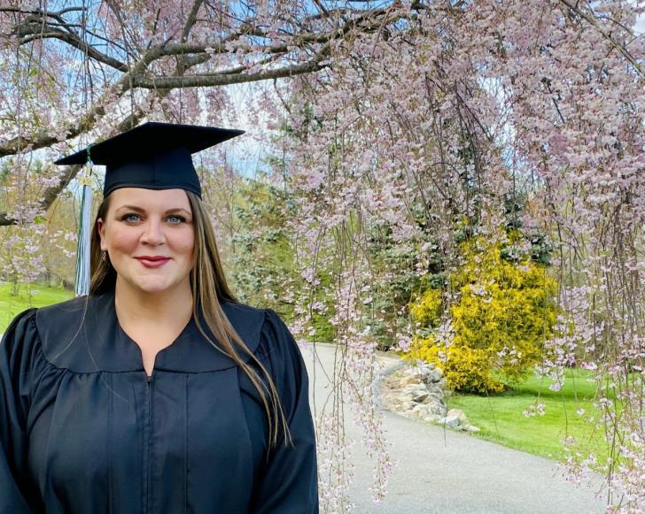 Alice Smith in graduation gown outside in front of blooming tree.