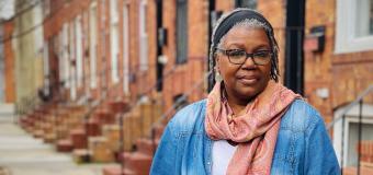 AJ Verdelle author photo standing on a sidewalk with brick row houses