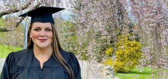 Alice Smith in graduation gown outside in front of blooming tree.