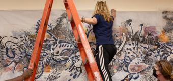 Woman on a ladder installing a piece of artwork