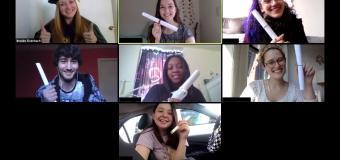 Screenshot of a Zoom call, students hold up paper rolled up to look like diplomas. Professor Eisenbach wears her regalia.