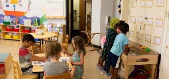 Young children paint and play at a sensory table in a classroom