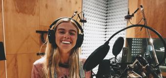 Carly Eaton in a music studio with headphones on standing in front of a mic