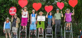 Group of people standing on step stools outside holding up red heart cutouts