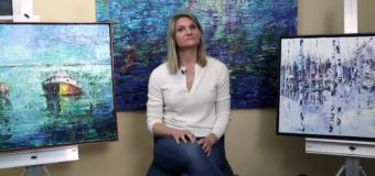 Julia Powell pictured in her studio surrounded by three paintings