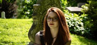 Katya Zinn sitting in the grass in a cemetery with a typewriter