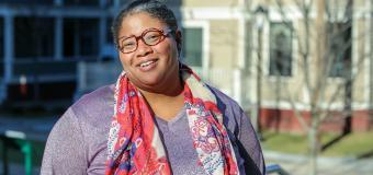 Kenish Coy poses in the sunshine on the Quad in a purple shirt and red-and-white scarf