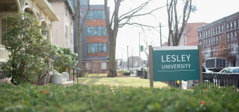 Photograph of admissions building shrubs and exterior with Lesley sign and sidewalk in the background.