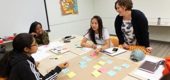 Students and a teacher sit around a table working on a project.
