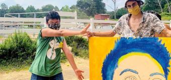 Portrait in progress of Jon Lopez-Wilen. Stands with a student, both are masked.