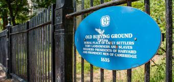 Blue plaque on the wrought iron cemetery fence reads: Old Burying Ground. Burial place of early settlers, tory landowners and slaves, soldiers, presidents of Harvard and prominent men of Cambridge.