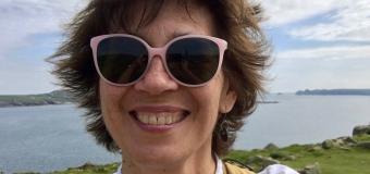 Pamela Petro with sunglasses and water in the landscape behind her. in wales.