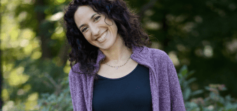 Rachel Kadish standing outside with purple shirt on, with her head tilted as she smiles at the camera