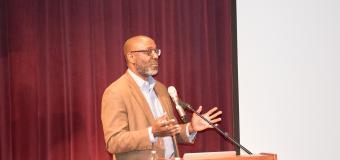 Trent Masiki speaks at a podium on the theater stage.